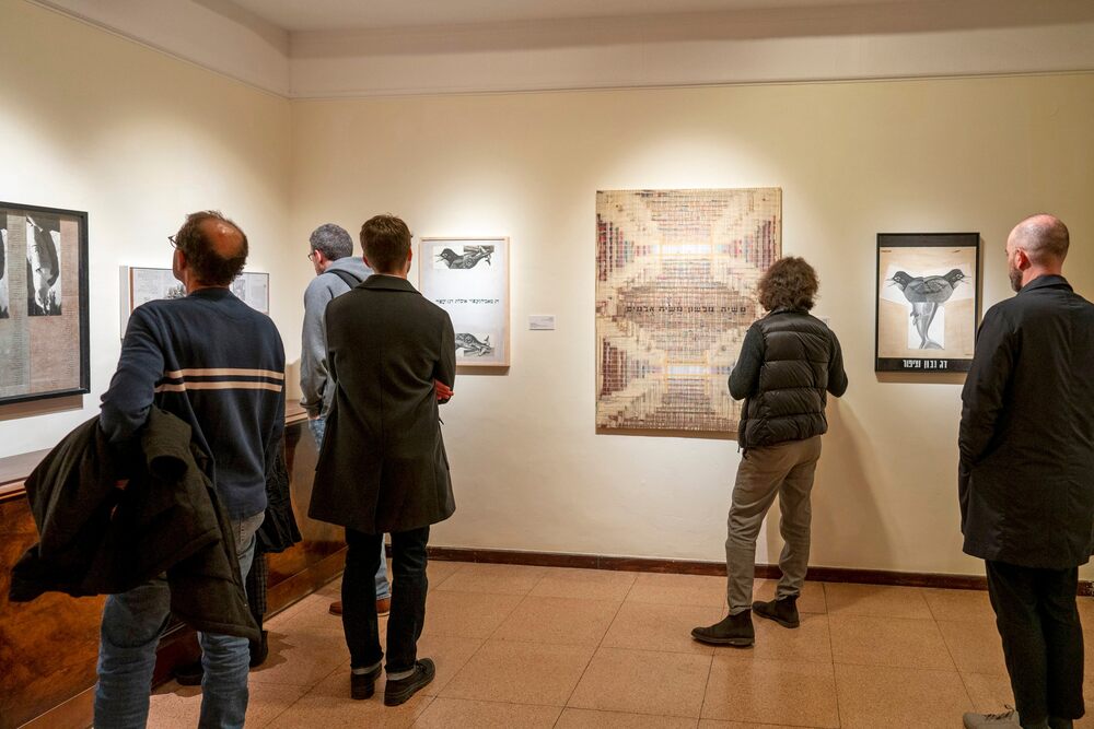 מבקרים פזורים בחלל מתבוננים בעבודות התערוכה התלויות על הקיר