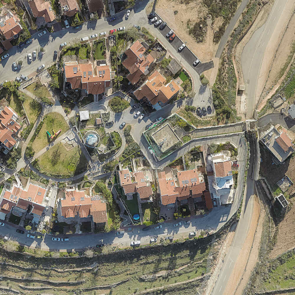 צילום של מיקי קרצמן ממבט על המשקיף על בתי ההתנחלות בעלי הגגות האדומים והמדשאות הירוקות הסובבות אותם, מקיפים את הבית הפלסטיני המרובע